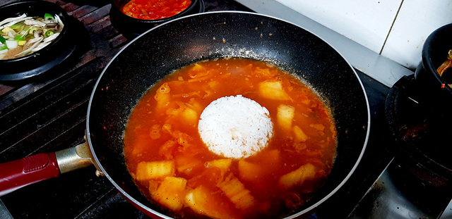 김치를 볶고 끓인 다음 식은 밥을 더하고 있다.