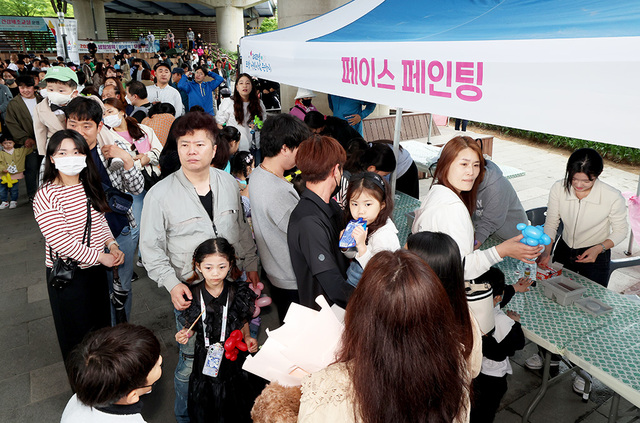 부모와 아이들이 다채로운 공연을 보며 페이스 페인팅 순서를 기다리고 있다.