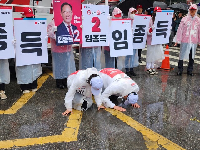 임종득후보 부부가 비가오는 가운데 시민들에게 큰 절을 올리고 있다.